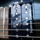 Detailní záběr na hриф elektrické kytary s dvěma černými humbuckery. Na pravém snímači je bílý nápis Seymour Duncan. Hриф má dřevěnou barvu s viditel…