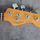 Fotografie zachycuje hlavu basové kytary z přírodního dřeva s čtyřmi kovovými ladičkami. Na dřevě je černý nápis Fender a pod ním menší text MADE IN…