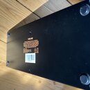 Spodní strana černého elektronického zařízení s gumovými nožičkami. Na spodku je bílý text, který obsahuje značku NUX a model MODEL: MG-30. Je zde ro…