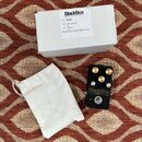 Na fotografii je černý efekt pedál s nápisem BlackBox a menším textem ve Snouse Electric Company. Pedál má tři zlaté ovládací knoflíky a jeden stoupa…