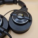 Černá uzavřená velká sluchátka z plastu. Na vnější straně mušle je vidět logo KRK SYSTEMS a pod ním označení modelu KNS-8400. Povrch plastu vykazuje…
