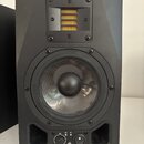 Černý studiový monitor s dvěma reproduktory. Horní výšek je žluté barvy a umístěn v černém rámu s viditelnými šrouby. Spodní středobasový reproduktor…