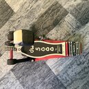 Červený bubnový pedál s černým šlapákem. Na šlapáku je bílý nápis dw 5000 a The Drummer's Choice. Na základní desce je vidět nápis dwdw dw. Povrch vy…