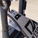 Detailní záběr na pedál bicího tahu v černé barvě s kovovým šlapadlem. Na horním bílém prvku je červené písmeno P a nápis POWER GLIC. Na šlapadle je…