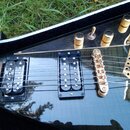 Černá elektrická kytara s kovovými zlatými prvky. Na obou snímačích je nápis Seymour Duncan. Kytara má tři zlaté otočné knofíky, jeden přepínač a zla…
