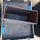 Černý obdélníkový box z dřevěného materiálu s tmavým povrchem, umístěný uvnitř transportního kufru. Kufr má hliníkové hrany a kovové zapínání, vnitřn…