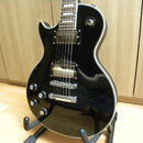 Černá elektrická kytara s tvarem single-cut a bílým lemováním kolem korpusu. Nástroj má dva humbuckery, Tune-o-matic kobylku a stoper. Na korpusu jso…