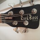 Fotografie zachycuje hlavu basové kytary v černé barvě s matným povrchem. Na hlavě je bílý nápis RockBass a pod ním menší text by Warwick. Na hmatník…