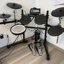 Elektronická bicí souprava s černým rámem a černými padovými plochami. Na bílém snare padu je nápis Roland a V-Drums, na modulu je značka Roland. Sou…
