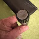 Detailní pohled na hlavu mikrofonu s kovovou mřížkou a ozubeným kroužkem kolem ní. Nástroj je stříbrné barvy a nemá žádné viditelné značky ani nápisy…