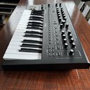 Černý synthesizér s bílými a černými klávesami. Na ovládacím panelu jsou viditelné nápisy moog a EVOLVER, množství otočných potenciometrů a tlačítek.…