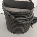 Černý kabel namotaný na kulatém černém cívce. Na horní části cívky je umístěna černá kovová lišta s řadou konektorů. Vedle cívky leží černý látkový v…