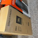 Na fotografii jsou dvě krabice od reproduktorů. Přední hnědá kartonová krabice nese nápisy EON615 POWERED, logo JBL a text PROFESSIONAL by HARMAN, dá…