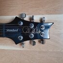 Černá hlava elektrické kytary s nápisem Standard a podpisem Paul Reed Smith. Na hlavě jsou umístěny šest chromovaných ladiček. Povrch je hladký a les…