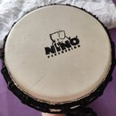 Kruhové perkusní nástroje s bílou membránou a černým obrubením. Uprostřed membrány je černý nápis NINO PERCUSSION s logem slona. Povrch membrány vyka…