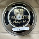 Kruhový reproduktor s kovovým rámem v šedé barvě. Na černém středovém krytu je zlatý nápis CELESTION LOUDSPEAKERS, G12, 8ohms a Vintage 30. Po obvodu…