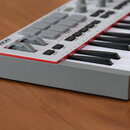 Šedý MIDI kontrolér s klávesnicí a červeným okrajem v horní části. Na levé straně je viditelné logo AKAI a pod ním nápis Professional Audio. Zařízení…