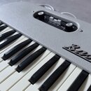 Šedý klavír s texturovaným povrchem a černobílými klávesami. Na pravé straně je nápis Bass 3. V horní části se nachází ovládací panel s dvěma otočným…