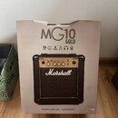 Kartonová krabice s obrázkem kytarového komba. Na krabici je nápis MG10 GOLD a logo Marshall, dále údaje 10 WATT, 6.5", 2 CHANNEL a ikony sluchátek a…