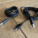 Dvě černé propojovací kabeláže s USB konektory. Jeden kabel má na koncích USB-C a USB-B, druhý kabel má konektory USB-A a USB-B. Kabely jsou svinuté…