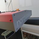 Detailní pohled na roh červeného syntetizátoru s šedým bočním panelem. Na šedém panelu je nápis nordwave2. Povrch nástroje vykazuje mírné opotřebení…