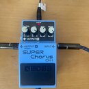 Modrý kytarový efekt s nápisy SUPER Chorus a CH-1. Na spodní části je černý spínací pedál s vyraženým logem BOSS. Na horní straně jsou čtyři ovládací…