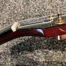 Detail hlavy kytary v tmavě červené barvě s viditnou strukturou dřeva. Na čele je zlatý nápis "Ibanez" a zlaté ladičky. Povrch lakovaného dřeva vykaz…