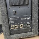 Zadní strana aktivního reproduktoru v šedém textilním potahu s černým kovovým zadním panelem. Na panelu je nápis ACTIVE SPEAKER SYSTEM, model ASS 500…