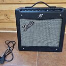 Černý kytarový kombozesilovač s šedou textilní maskou reproduktoru. Na masce je bílý nápis Fender a nad ní se nachází malé kulaté logo. Horní panel o…