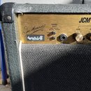 Detail kytarového komba s černým vinylovým potahem a zlatým předním panelem. Na panelu je nápis JCM, podpis Jim Marshall a označení CHANNEL SELECT s…