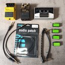 Fotografie zobrazuje tři kytarové efekty, balení patch kabelů a čtyři samostatné krátké kabely. Žlutý pedál má nápisy Bass OverDrive ODE-3 a BOSS, če…