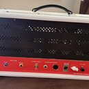 Zadní strana kytarového zesilovače s bílým povrchem a červeným panelem konektorů. Na panelu jsou nápisy SERIAL LOOP (SEND, RETURN), OUTPUT SELECT (4…