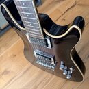 Černá elektrická kytara s bílým lemováním kolem korpusu. Nástroj má dva humbuckery, chromovaný most s páčkou vibrata a tři ovládací knofíky. Povrch l…