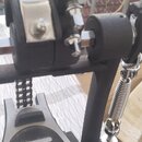 Detailní záběr na černý kovový mechanismus s chromovanými prvky a řetězem. Na komponentech nejsou žádné viditelné značky ani nápisy. Povrch černého l…