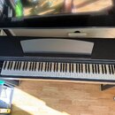 Černý digitální piano v černém dřevěném korpusu s bílými a černými klávesami. Nástroj je umístěn v interiéru na dřevěné podlaze. Na povrchu nejsou vi…