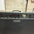 Černý kytarový kombozesilovač s černým textilním maskováním reproduktoru. Na předním panelu jsou ovládací knofíky s popisky GAIN, TREBLE, MID, BASS,…