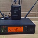 Černý bezdrátový přijímač s nápisem LD SYSTEMS WS1000G2R UHF PLL DIVERSITY WIRELESS RECEIVER a oranžovým displejem zobrazujícím hodnotu 826.300 MHz.…