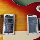 Detail elektrické kytary s červeno-žlutým přechodem (sunburst) a krémovým pickguardem. Na kytaru jsou instalovány dva snímače s kovovými kryty, z nic…