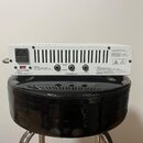 Zadní strana bílého zesilovače s ventilací v horní části. Jsou zde nápisy „1X8Ω“, „2X16Ω“, „16Ω“ a „SPEAKER OUT“. V pravém horním rohu je text „REMOV…