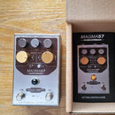 Stříbrný kytarový efekt s nápisy MAGMA57 a AMP VIBRATO & DRIVE. Na spodní části je logo ORIGIN EFFECTS, přepínač VIBE / ON a sériové číslo SER 0650.…