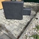 Dvě černé obalové brašny z syntetického materiálu umístěné na dlažbě. Větší brašna je v popředí a má nahoře úchyt, menší brašna v pozadí vykazuje na…