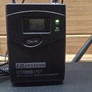 Černý bezdrátový vysílač s LCD displejem a tlačítkem MUTE. Na spodní části je nápis LD SYSTEMS, model WS1000G²BP a text UHF PLL DIVERSITY BODYPACK TR…
