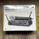 Fotografie znázorňuje krabici s bezdrátovým mikrofonním systémem. Na obalu je nápis CONCERT HANDHELD Frequency-Agile UHF Wireless System a logo SAMSO…