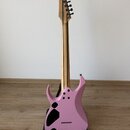 Růžová elektrická kytara s matným povrchem a přírodním dřevěným hmatníkem. Na hlavě nástroje je viditelný nápis "Schecter". Kytara stojí v černém sto…