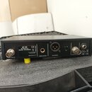 Černý elektronický přístroj s kovovým šasi umístěný v přepravním kufru z pěnového materiálu. Na zadní straně jsou konektory s popisky ANTENNA B, UNBA…