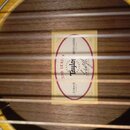 Detail vnitřku akustické kytary s viditelnou štítkovou nálepkou. Na štítku je uveden nápis 200 SERIES, logo Taylor GUITARS a model MODEL 214ce-N. Je…