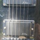 Detail elektrické kytary s černým povrchem a dvěma humbuckery. Na obou snímačích je bílý nápis B C Rich. V dolní části je vidět chromovaný kobylník s…
