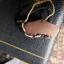 Měděný kovový kryt s vyvedenými elektrickými vodiči v žlutém a černém oplocení. Na povrchu je vyryto logo MM. Kryt vykazuje známky oxidace a povrchov…