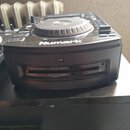 Černý DJ kontrolér s kruhovým jog-wheelem a ovládacími tlačítky. Na přední straně je viditelný bílý nápis Numark. Zařízení vykazuje mírné znečištění…