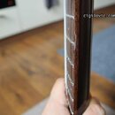 Detailní pohled na hриф strunového nástroje z tmavého dřeva. Na hraně hрифu jsou vidět kovové pražníky a bílé značky vpravo. V pravém horním rohu je…